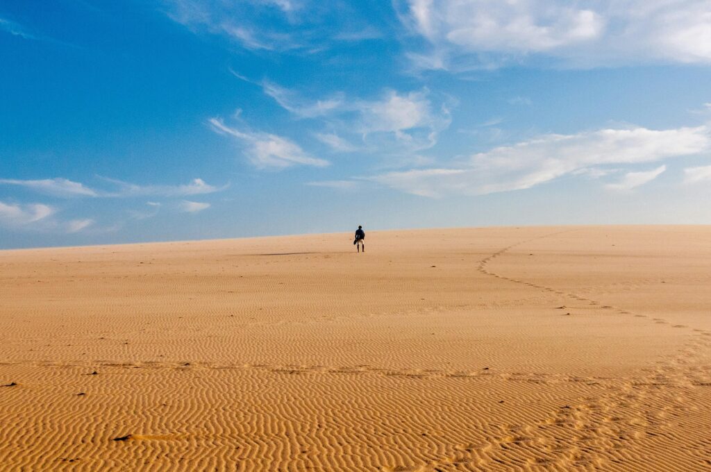 pexels-photo-1824570-1824570 A lone traveler walks across a vast and serene desert under a bright blue sky.