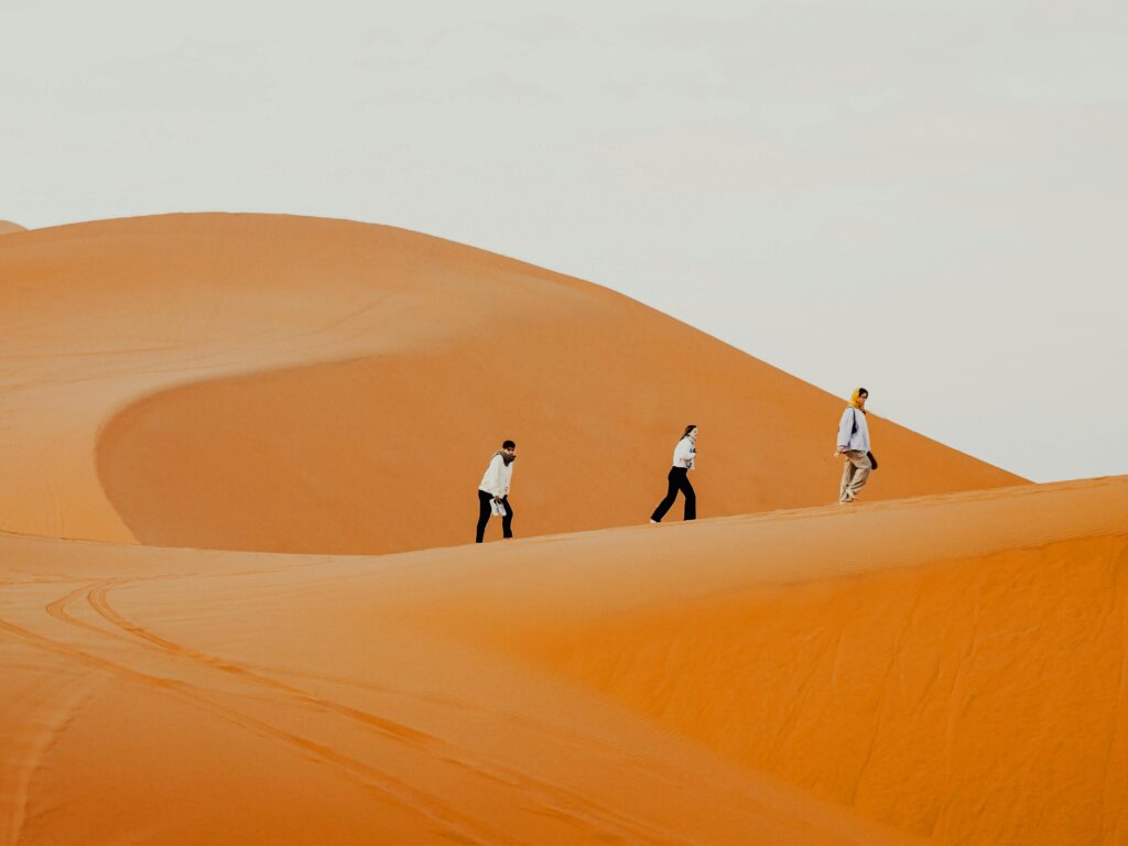 Three individuals walking on the vast orange sand dunes in Marrakesh, Morocco